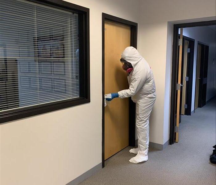 Technician wearing white Tyvek suit wiping down a doorknob