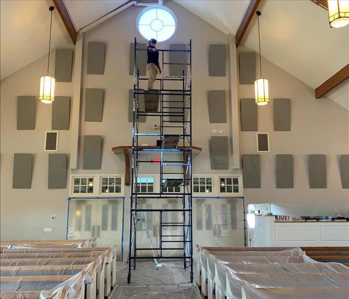 Technician on scaffolding near sealed church entrances between polyethylene-covered pews