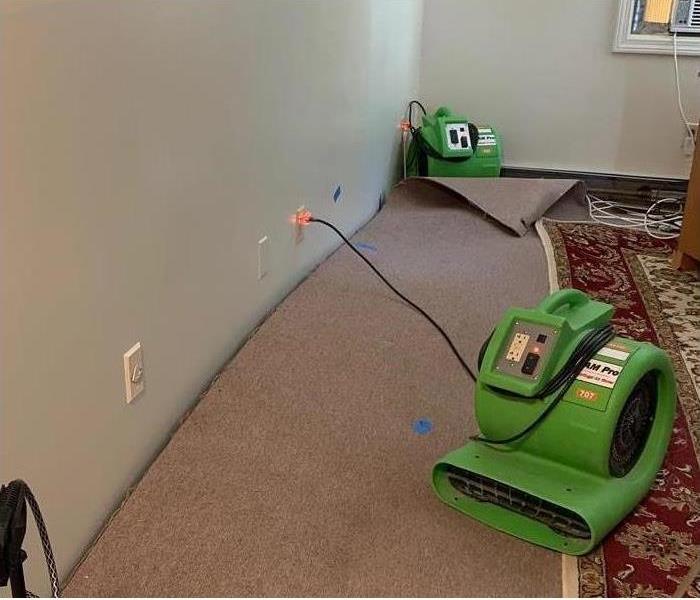 A room with the carpet lifted, with SERVPRO equipment 0n the carpet.